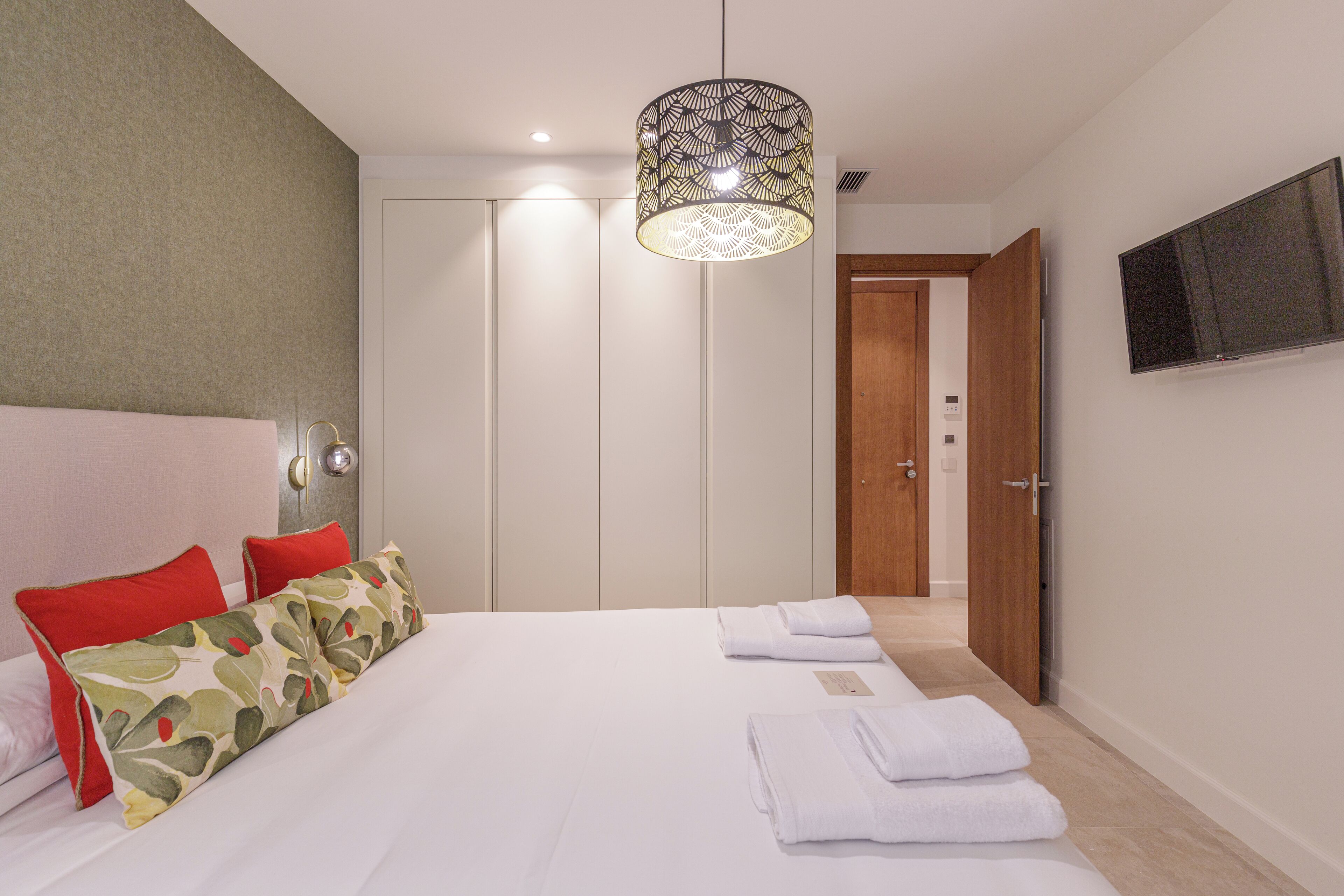 A hotel room with a bed, pillows, a TV, a wardrobe, and a door.