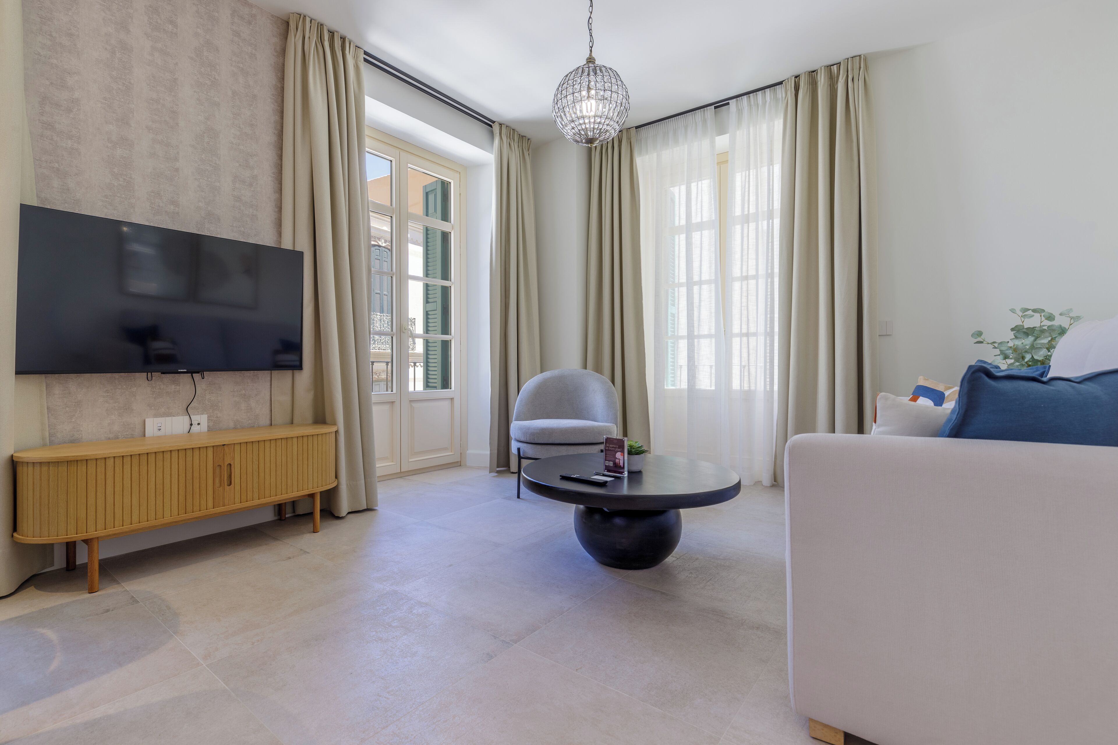 A modern living room with a flat-screen TV, a round coffee table, a grey armchair, and a sofa.