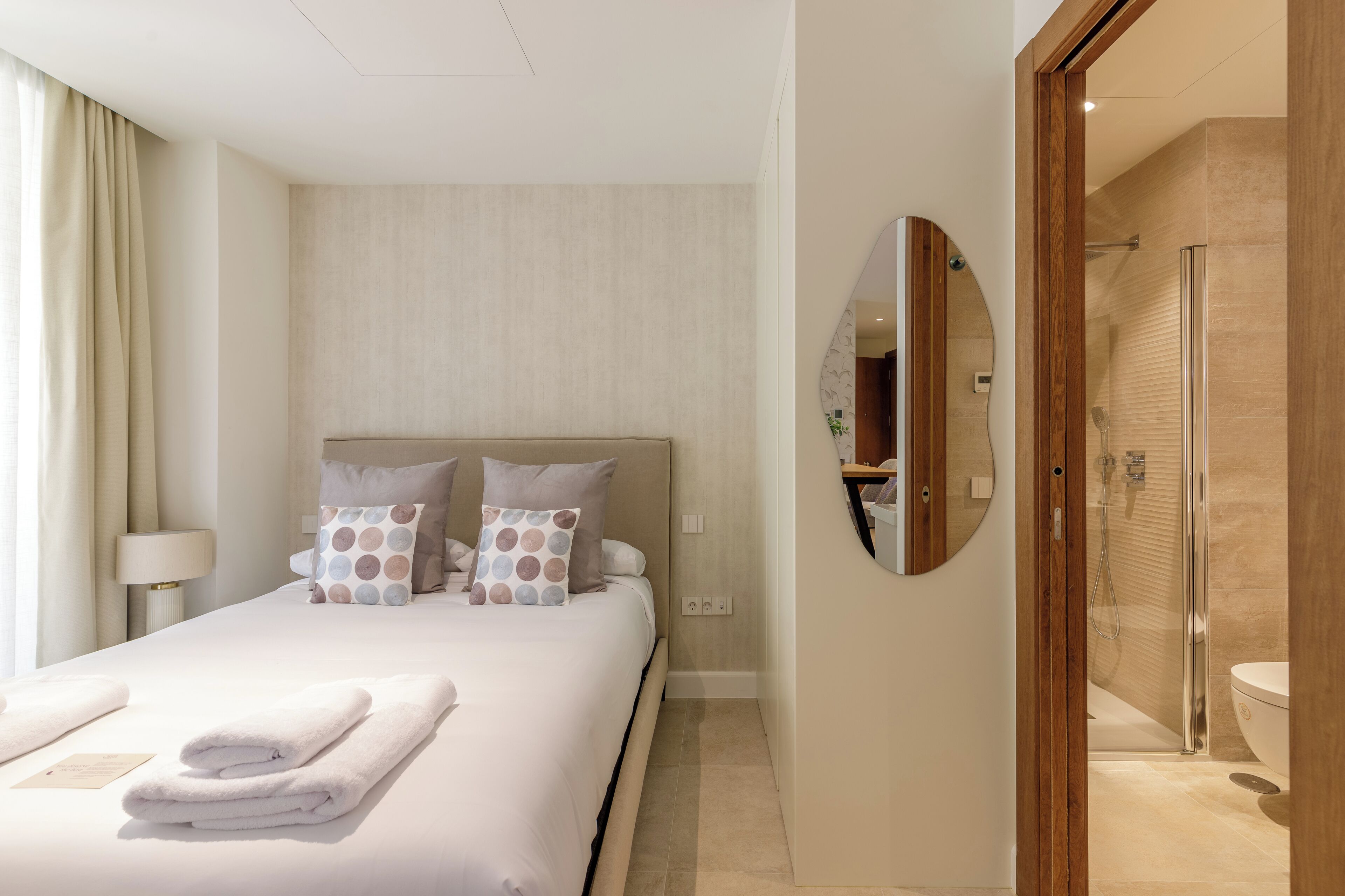 Una habitación de hotel con una cama bien hecha, un espejo grande y una zona de ducha.