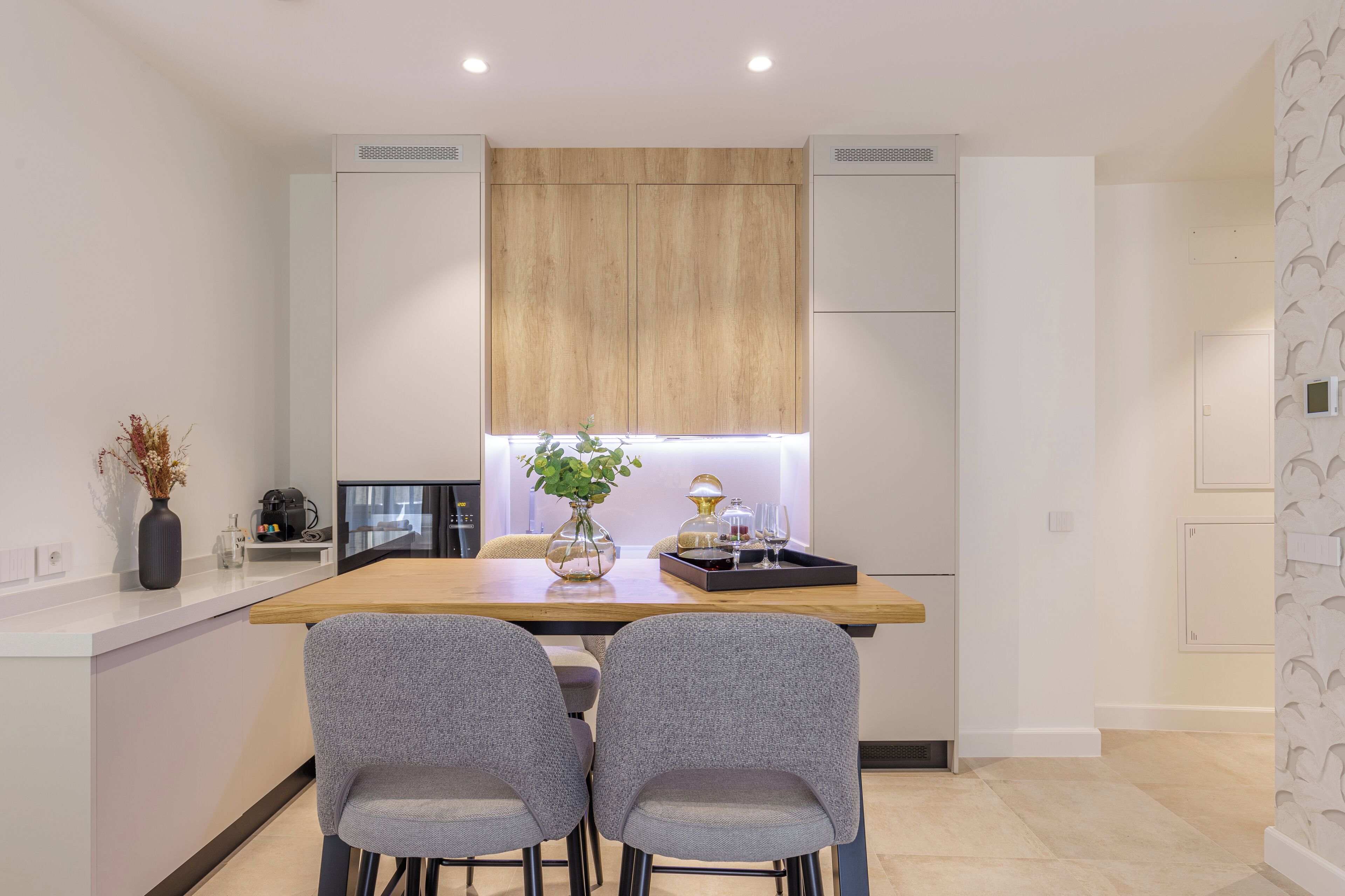 A modern kitchen with a central island, two grey chairs, and a wooden ceiling panel.