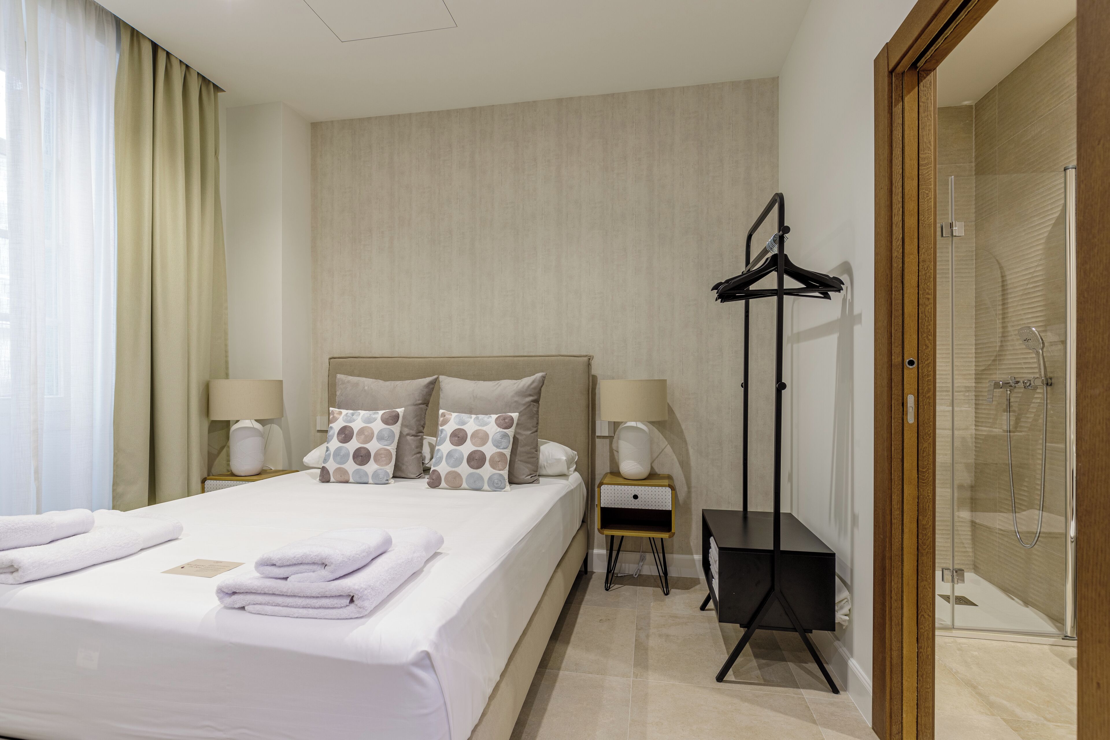 A hotel room with a bed, bedside tables, a wardrobe, and a shower area.