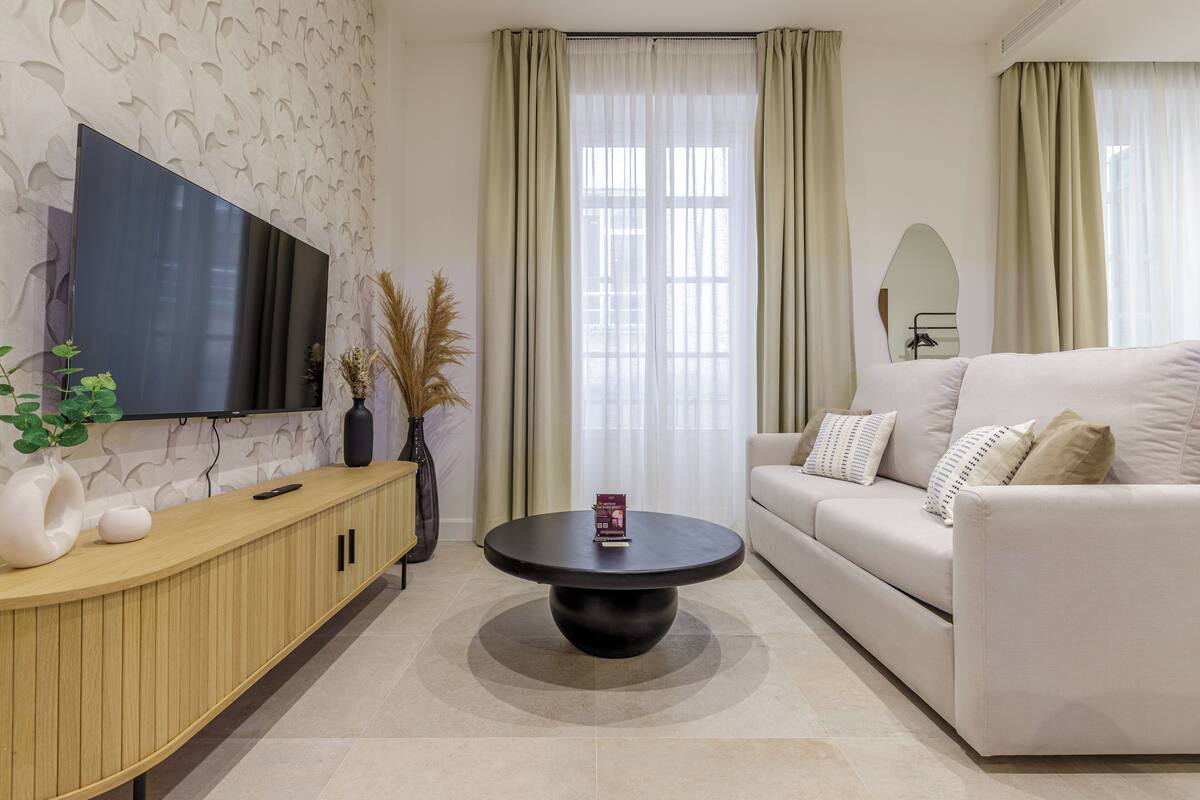 Un salon moderne avec un téléviseur à écran plat, une table basse ronde, un canapé et un vase décoratif.