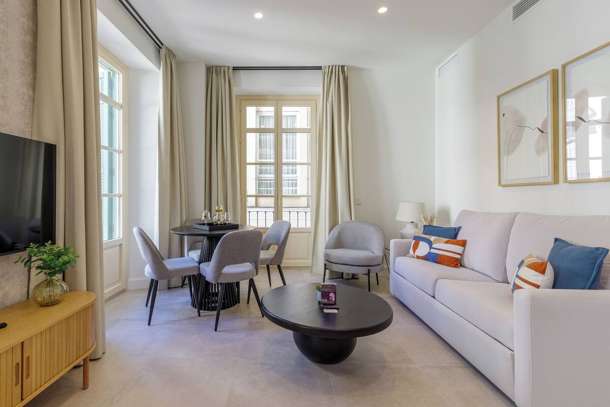 Un salon moderne comprenant un canapé, des fauteuils, une table basse, un téléviseur et un coin repas avec une table et des chaises.