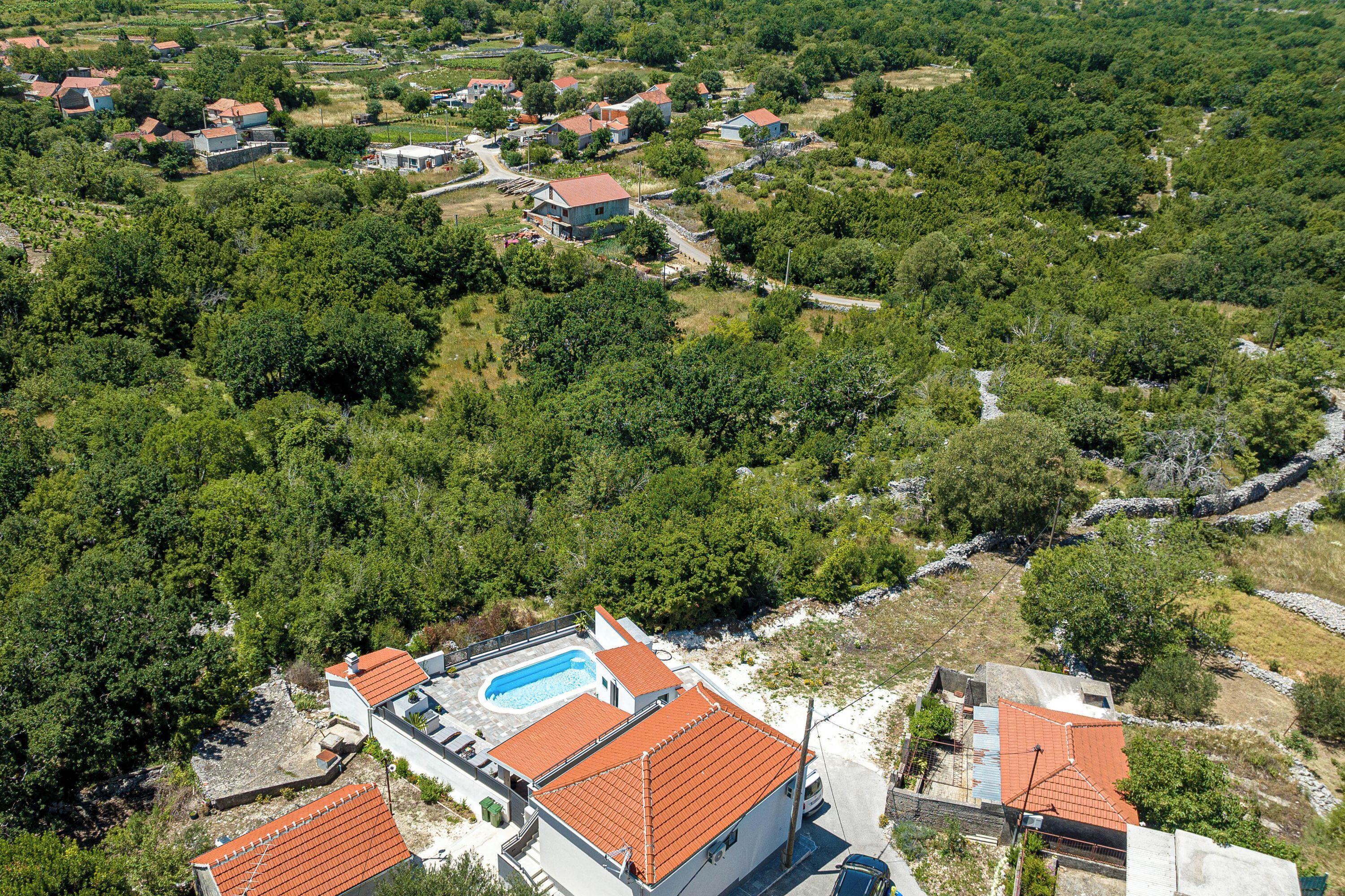 An aerial view of a residential area with houses, a swimming pool, and surrounding greenery.