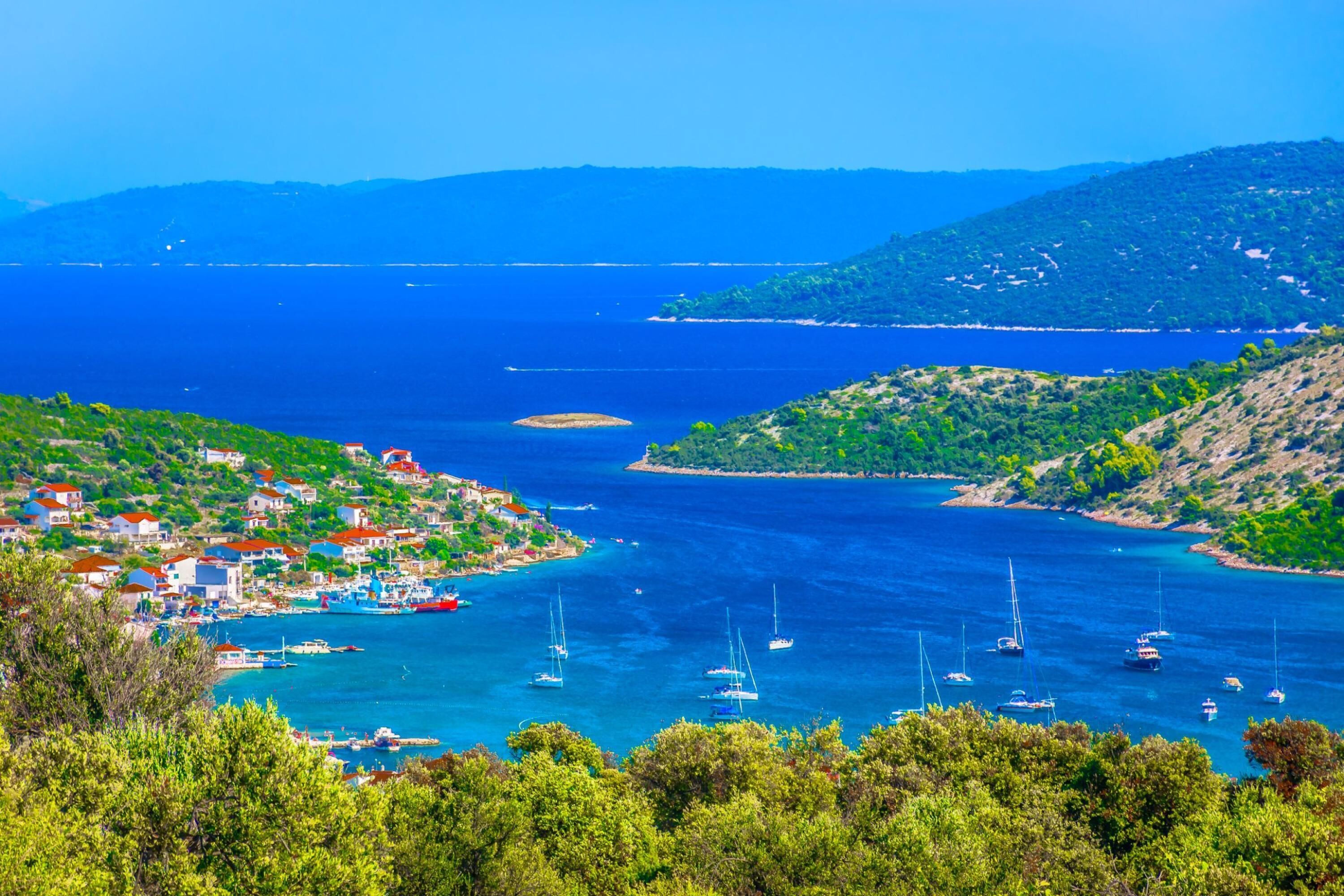 A coastal town with boats in the water, surrounded by greenery and hills.