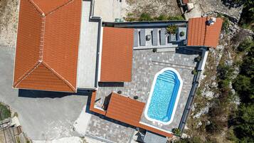 An aerial view of a property with a swimming pool, multiple rooms with tiled roofs, and outdoor seating areas.