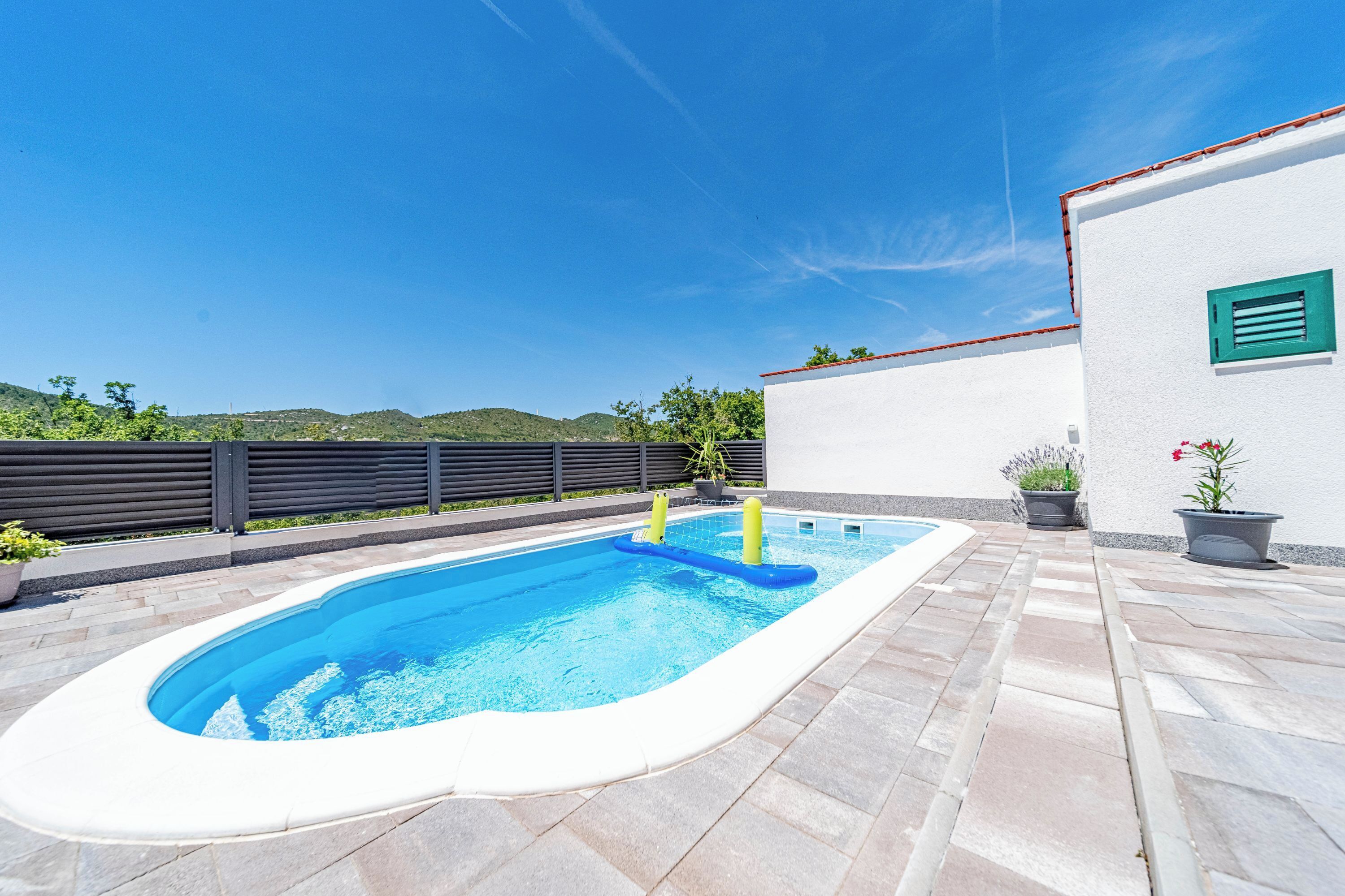 A swimming pool with a white interior, surrounded by stone tiles, and a view of hills in the background.