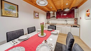 Un comedor con mantel rojo, platos blancos y un jarrón con flores. Hay sillas negras y techo de madera.