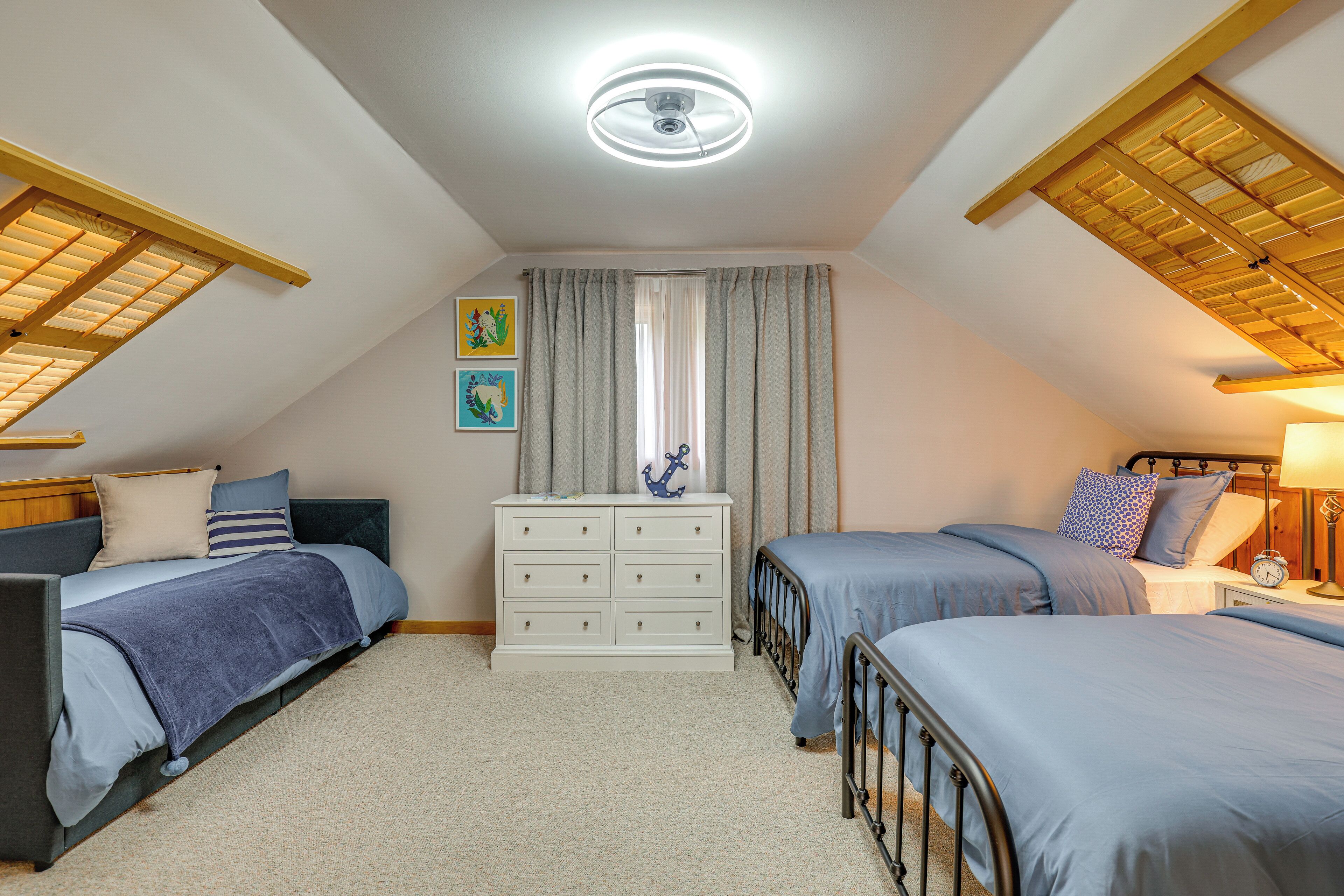 Quarto com duas camas, cômoda e ventilador de teto.