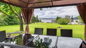 A covered outdoor seating area with a table and chairs, overlooking a grassy landscape and a body of water.