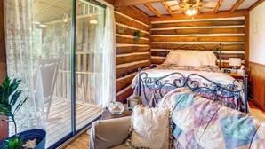 A log cabin bedroom with a bed, a chair, a small table, and a potted plant.