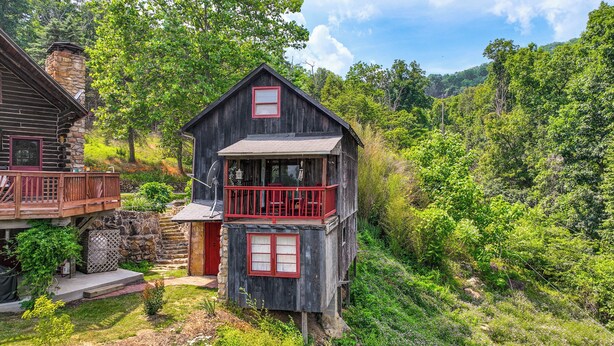 A rustic cabin with a stone chimney, a red balcony, and a small porch.