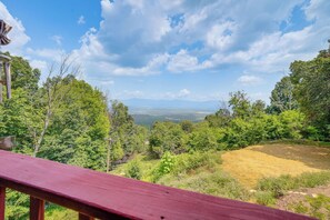 A wooden deck overlooking a lush landscape with dense trees and a distant mountain range. - Cozy Luray Cabin w/ Views: Near Hiking Trails! (Luray)