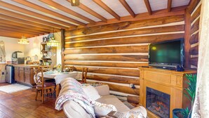 A cozy cabin interior with a dining area, sofa, fireplace, and television.