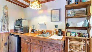 A kitchen with wooden cabinets, a sink, a microwave, and a wooden shelf with various kitchen items.