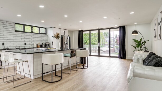 A modern kitchen with a central island, bar stools, and a dining area with a white sofa and a plant. - Lakefront Lynnwood Home w/ Balconies & Shared Dock (Lynnwood)