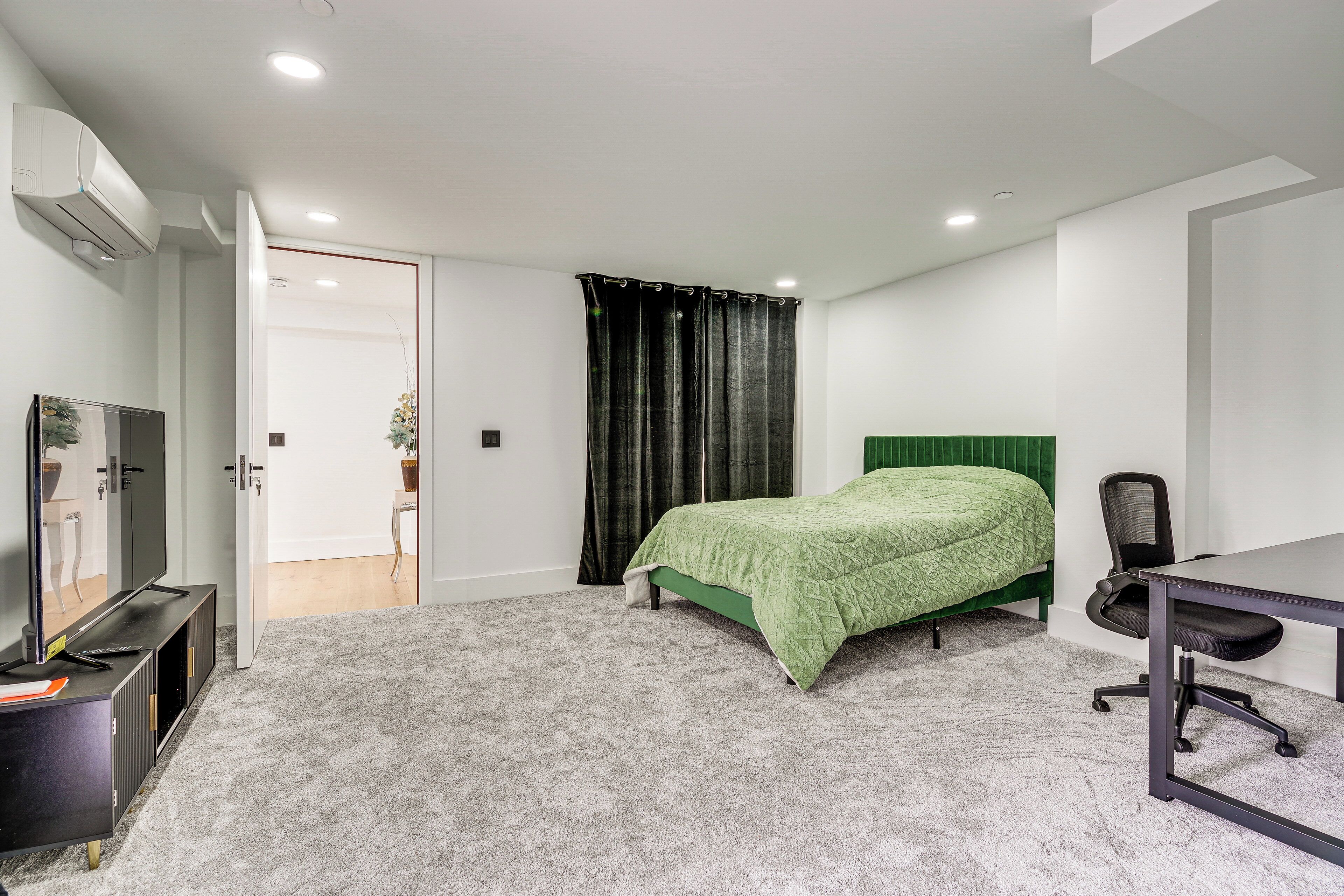 A bedroom with a bed, a desk, a chair, a TV, and an air conditioning unit.