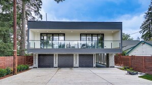 A modern two-story house with a balcony, large garage doors, and a concrete driveway. - Lakefront Lynnwood Home w/ Balconies & Shared Dock (Lynnwood)