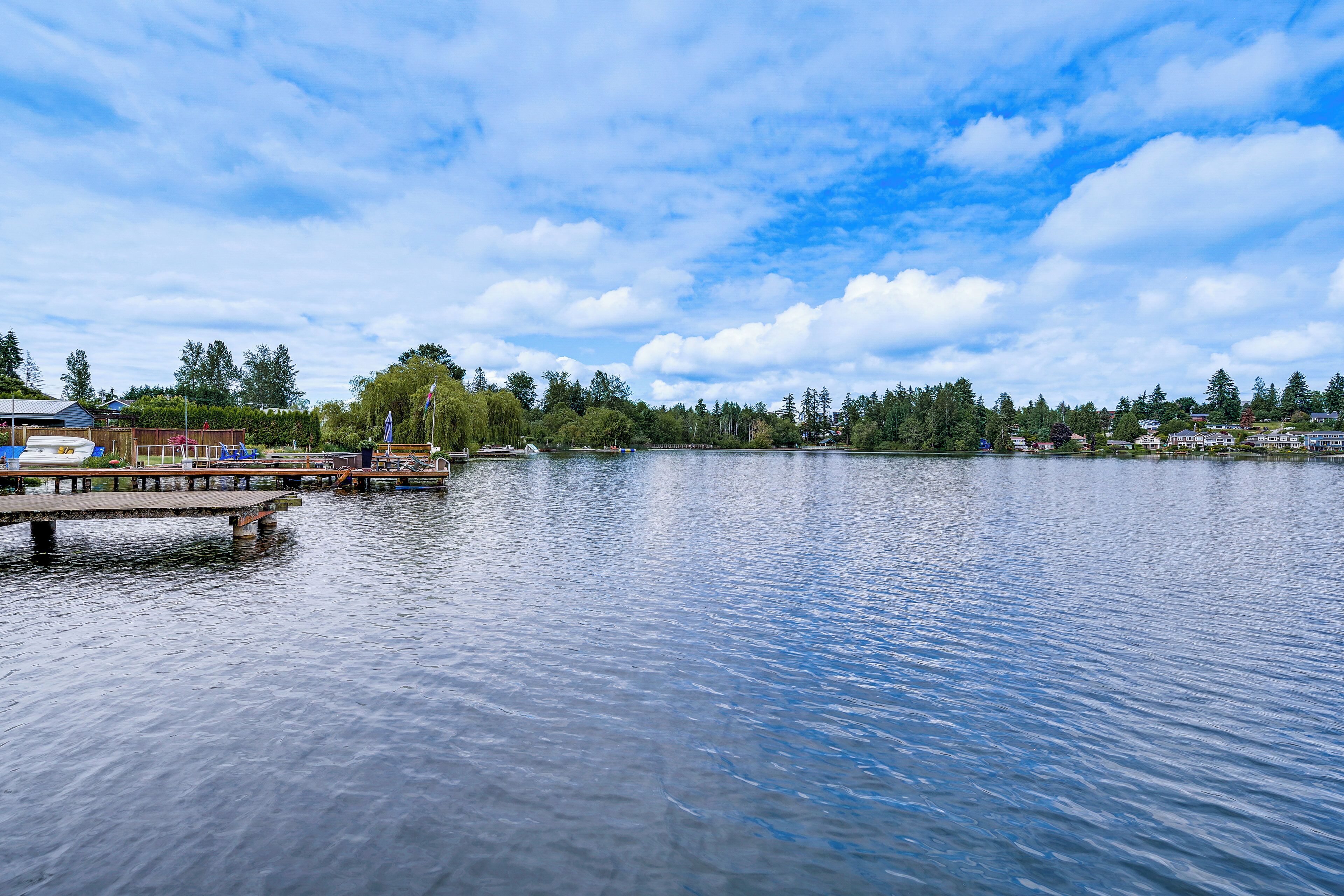 Ein ruhiger See mit einem Steg und einer Reihe von Häusern im Hintergrund.