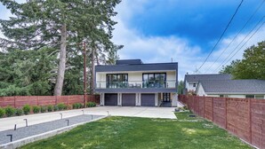 A modern two-story house with a large front yard, a wooden fence, and a driveway. - Lakefront Lynnwood Home w/ Balconies & Shared Dock (Lynnwood)