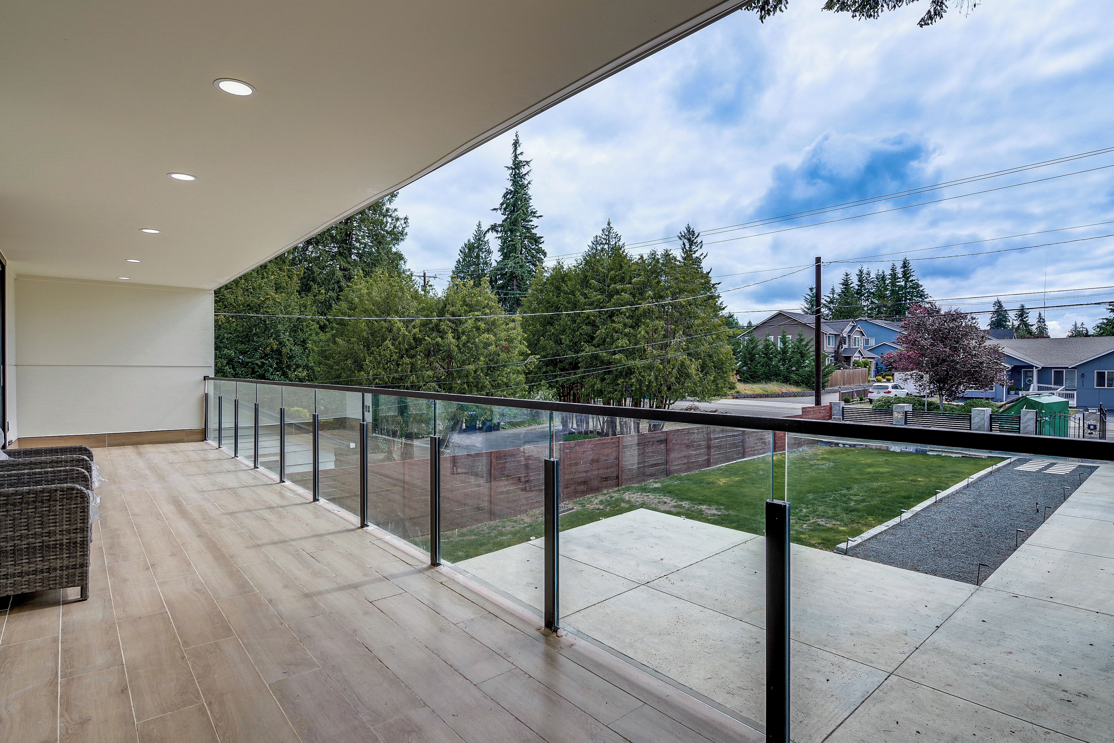 Un balcon doté d’une rambarde en verre, d’un plancher en bois et offrant une vue sur un quartier résidentiel avec des maisons et des arbres.