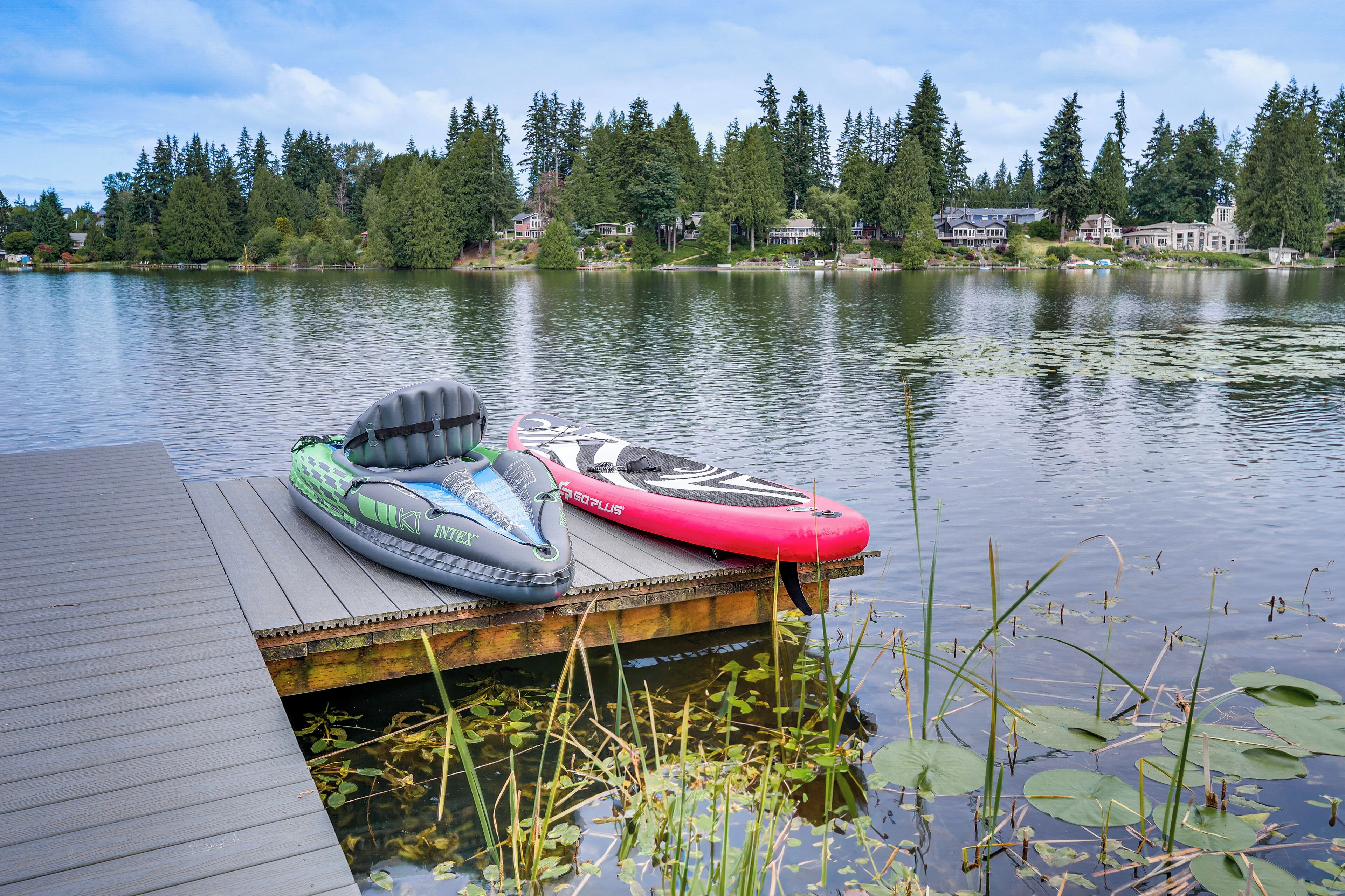 A wooden dock with two inflatables on it, overlooking a calm lake with houses in the background.