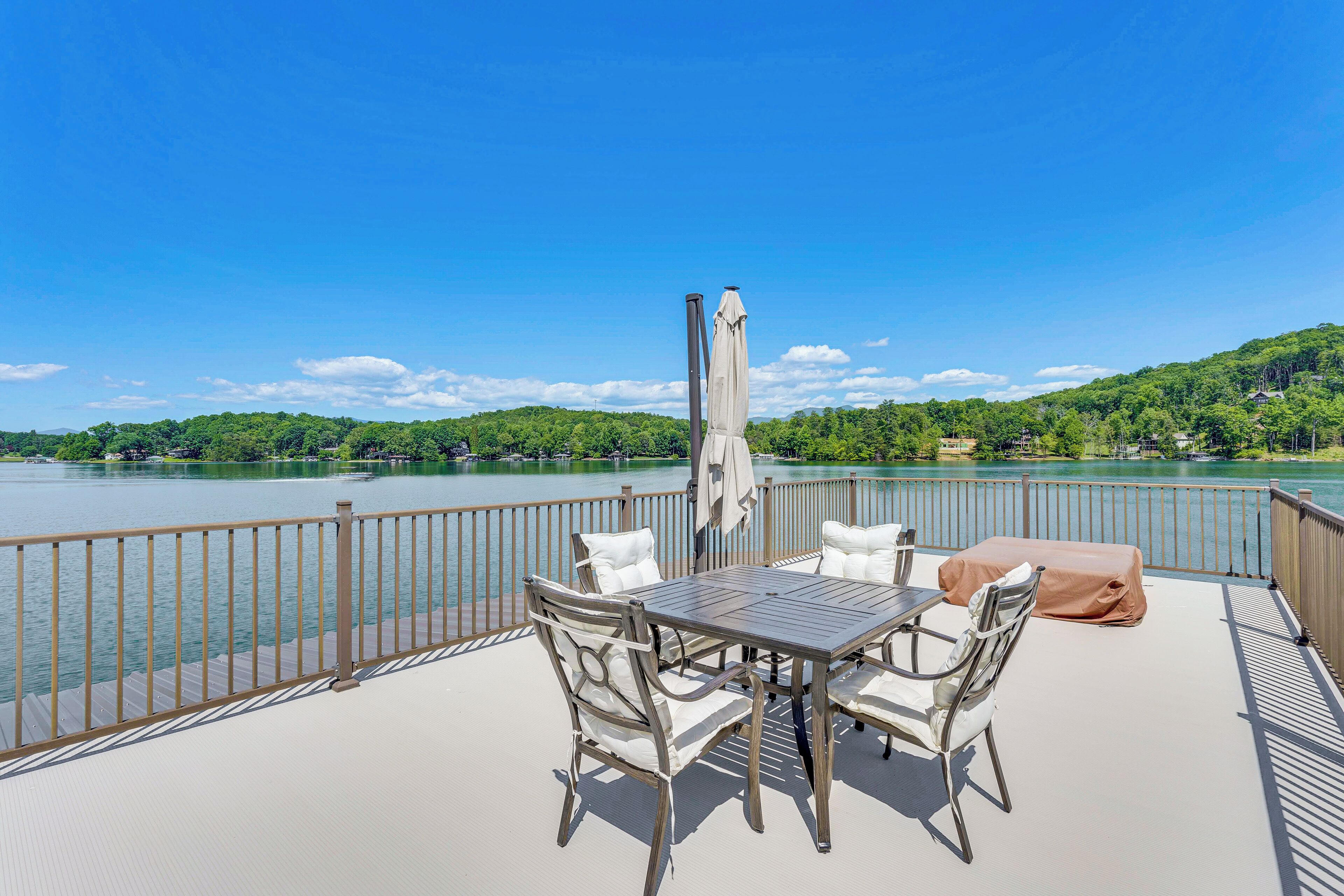 Eine Terrasse mit Tisch und Stühlen mit Blick auf einen See, im Hintergrund ein bewaldeter Hügel.