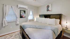 A bedroom with a bed, a ceiling fan, an air conditioner, a nightstand, and a wall-mounted artwork. - Hot Springs Home w/ Yard, Walk to Bathhouse Row! (Hot Springs)