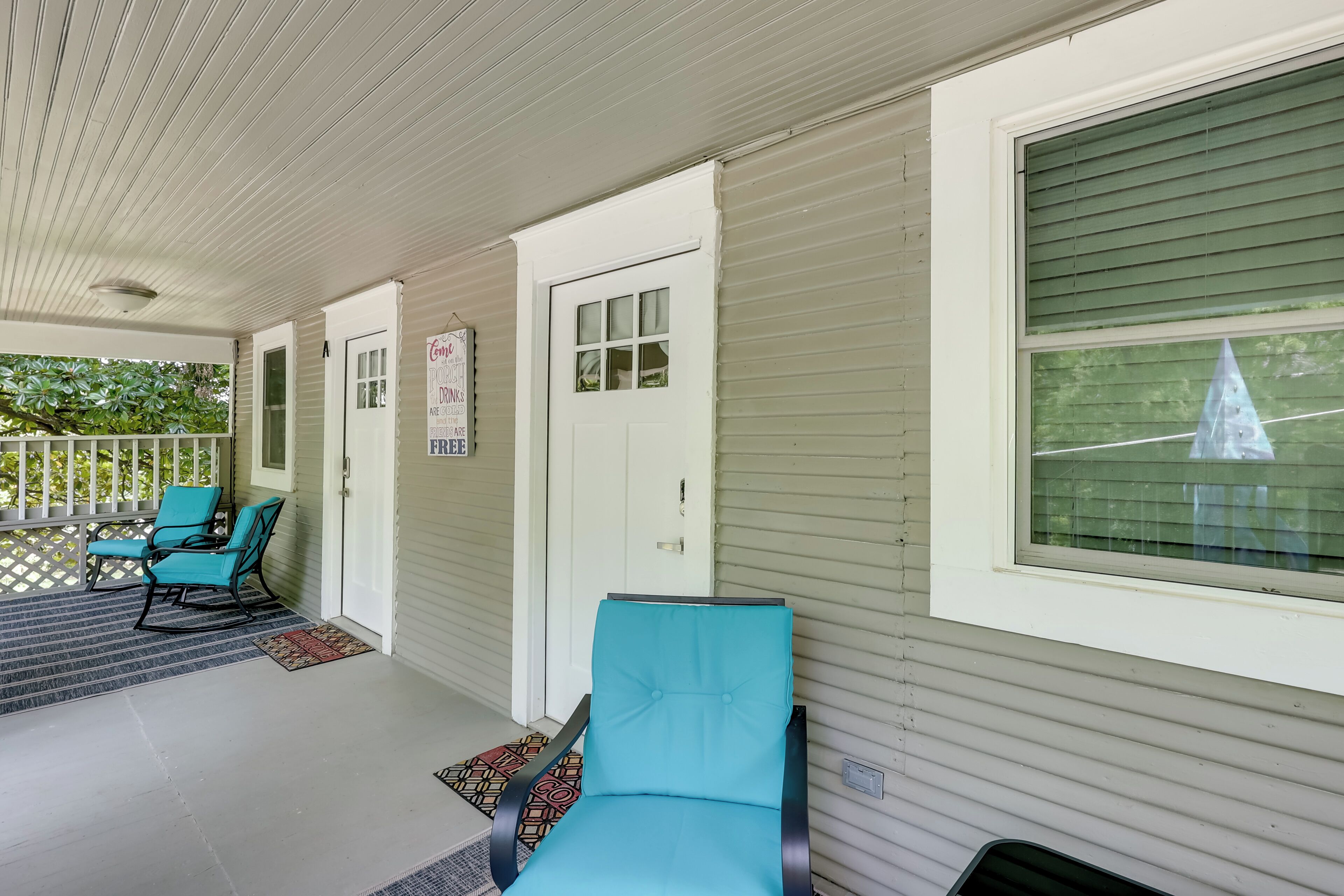 A covered porch with two blue chairs, a white door, and a window with blinds.