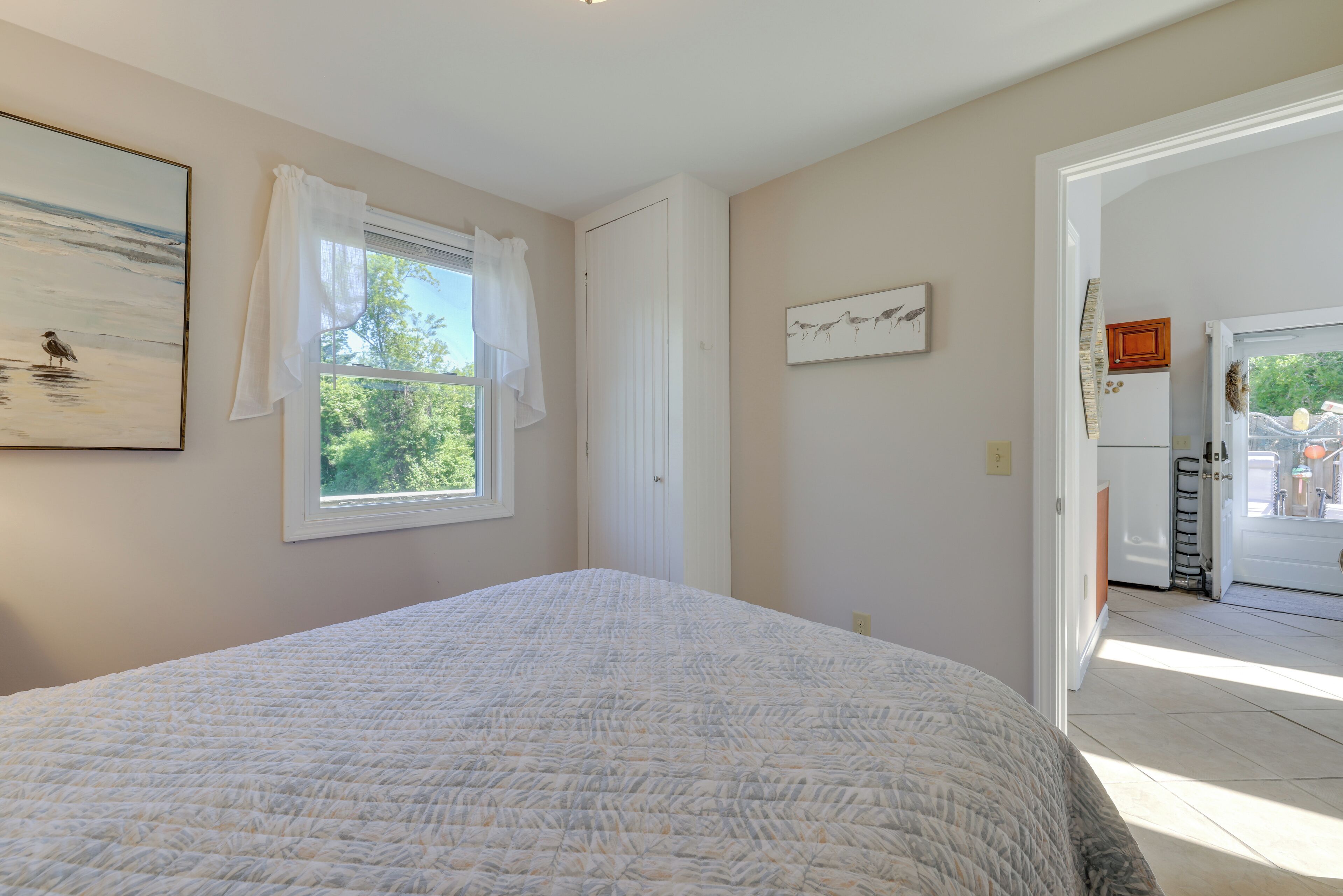 Een slaapkamer met een groot bed, een raam met witte gordijnen, een deur en uitzicht op buiten.