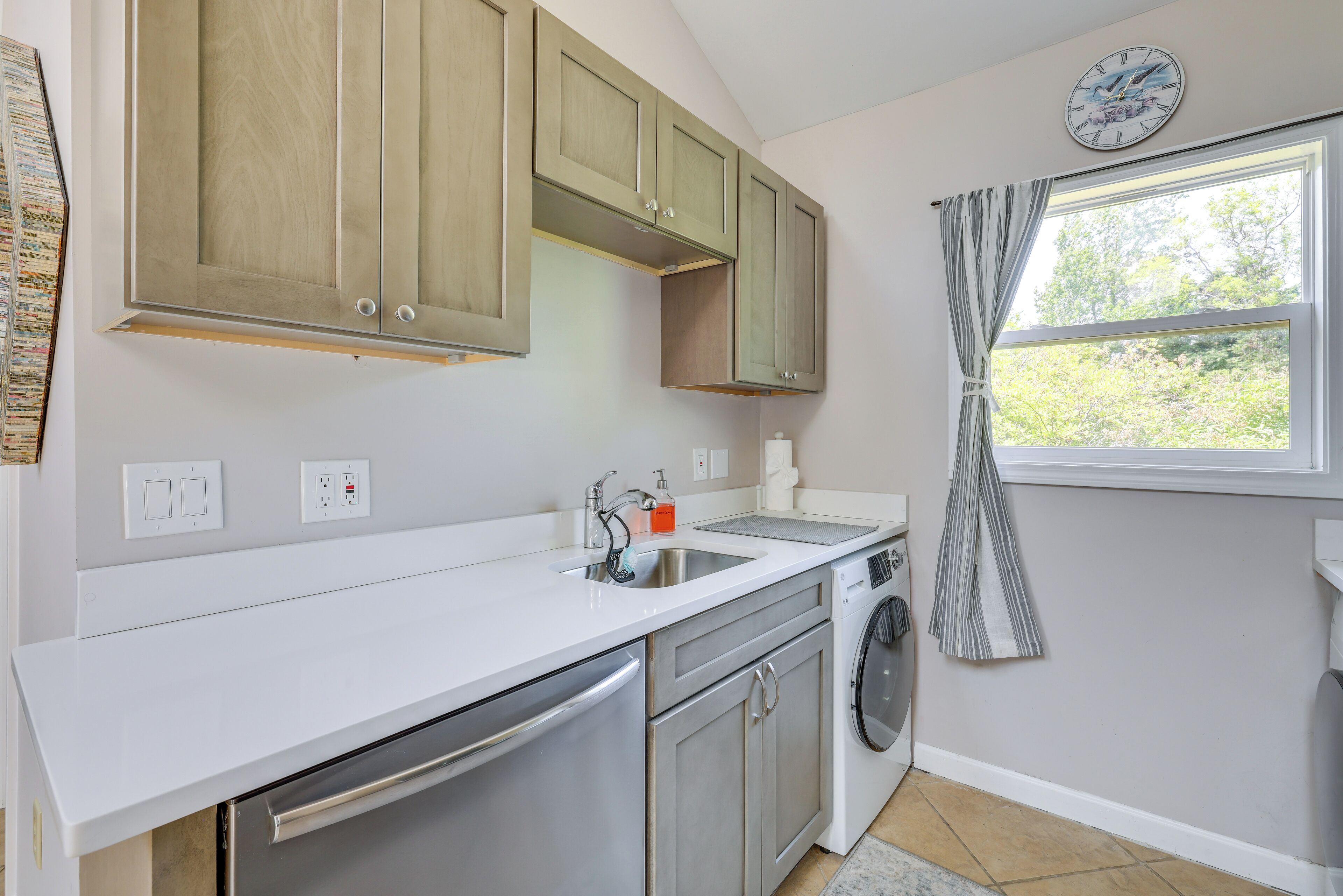 A kitchen with a dishwasher, washing machine, and a window with curtains.