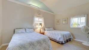 A bedroom with two beds, a bedside table with a lamp, a clock on the wall, and a window with curtains.