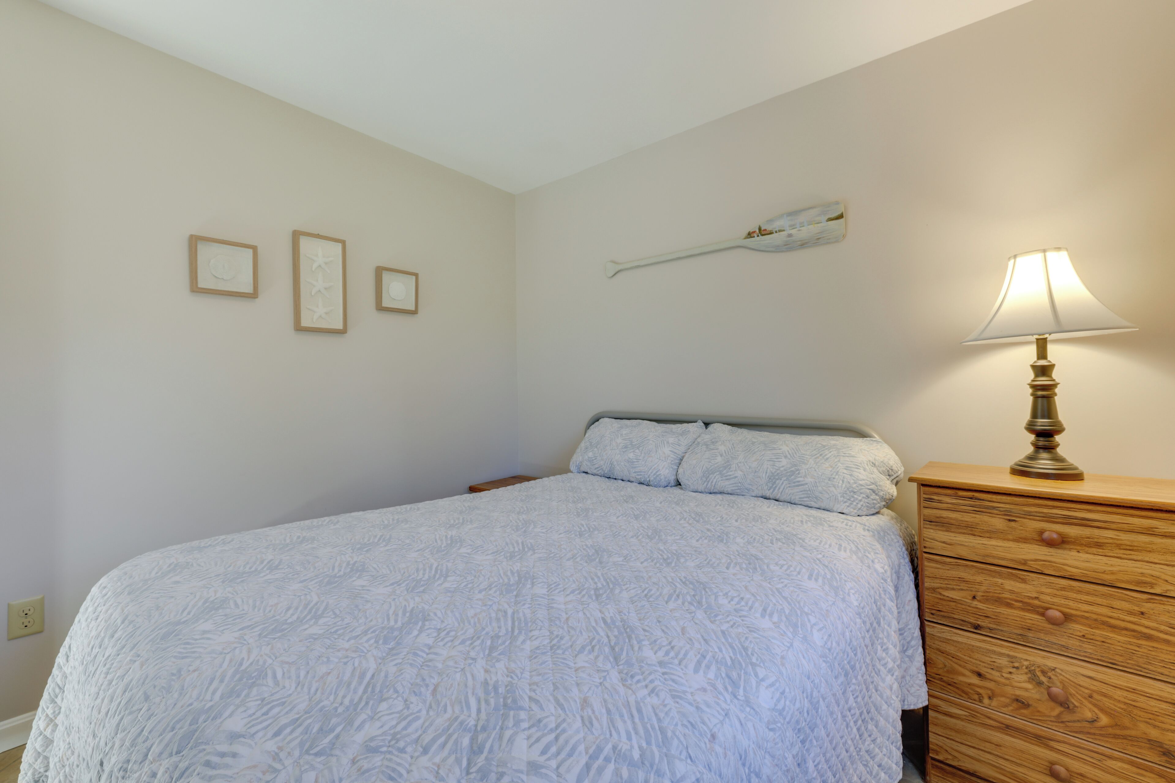A bedroom with a bed, a wooden dresser, and a wall-mounted lamp.