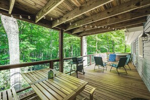A wooden deck with a table and chairs, overlooking a forested area. - Creek View + Hot Tub: Woodsy Maggie Valley Cottage (Maggie Valley)