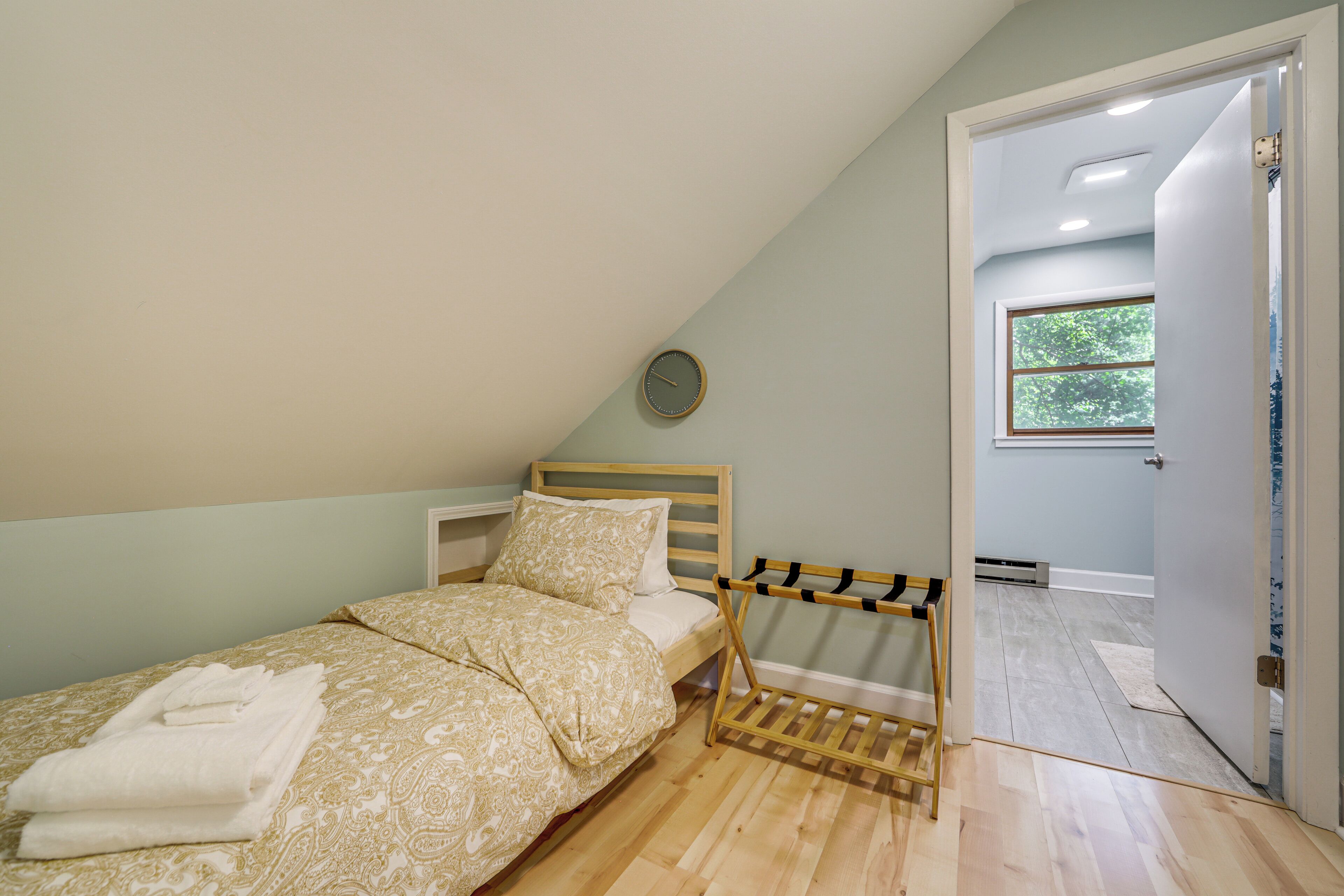 A bedroom with a bed, a wooden bench, a wall clock, and a window.