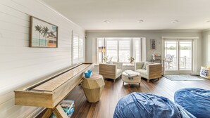 Ein geräumiges Wohnzimmer mit einer hölzernen Bank, einem Sofa und einem Couchtisch. Ein großes Fenster mit Jalousien, eine Tür zum Balkon und ein Gemälde an der Wand sind ebenfalls vorhanden.