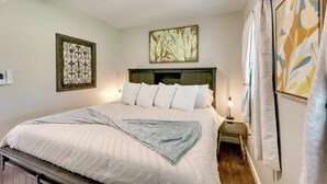 A neatly made bed with a white comforter and a blue throw blanket, a bedside table with a lamp, and a wall-mounted air conditioner. - Pet-friendly Home, Near Hot Springs National Park! (Hot Springs)