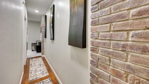 A hallway with a brick wall, white walls, and a wooden floor. - Pet-friendly Home, Near Hot Springs National Park! (Hot Springs)