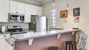 A kitchen with white cabinets, stainless steel appliances, granite countertops, and a bar area with stools. - South Padre Island: Pool Access, 1 Block to Beach! (South Padre Island)