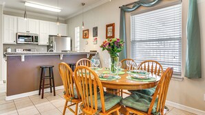 A kitchen with white cabinets, a microwave, and a refrigerator. There is a dining table with chairs and a vase of flowers. - South Padre Island: Pool Access, 1 Block to Beach! (South Padre Island)