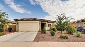 Ein eingeschossiges Haus mit einer beige farbenen Garagentür, umgeben von angelegten Gartenbeeten und kleinen Sträuchern.