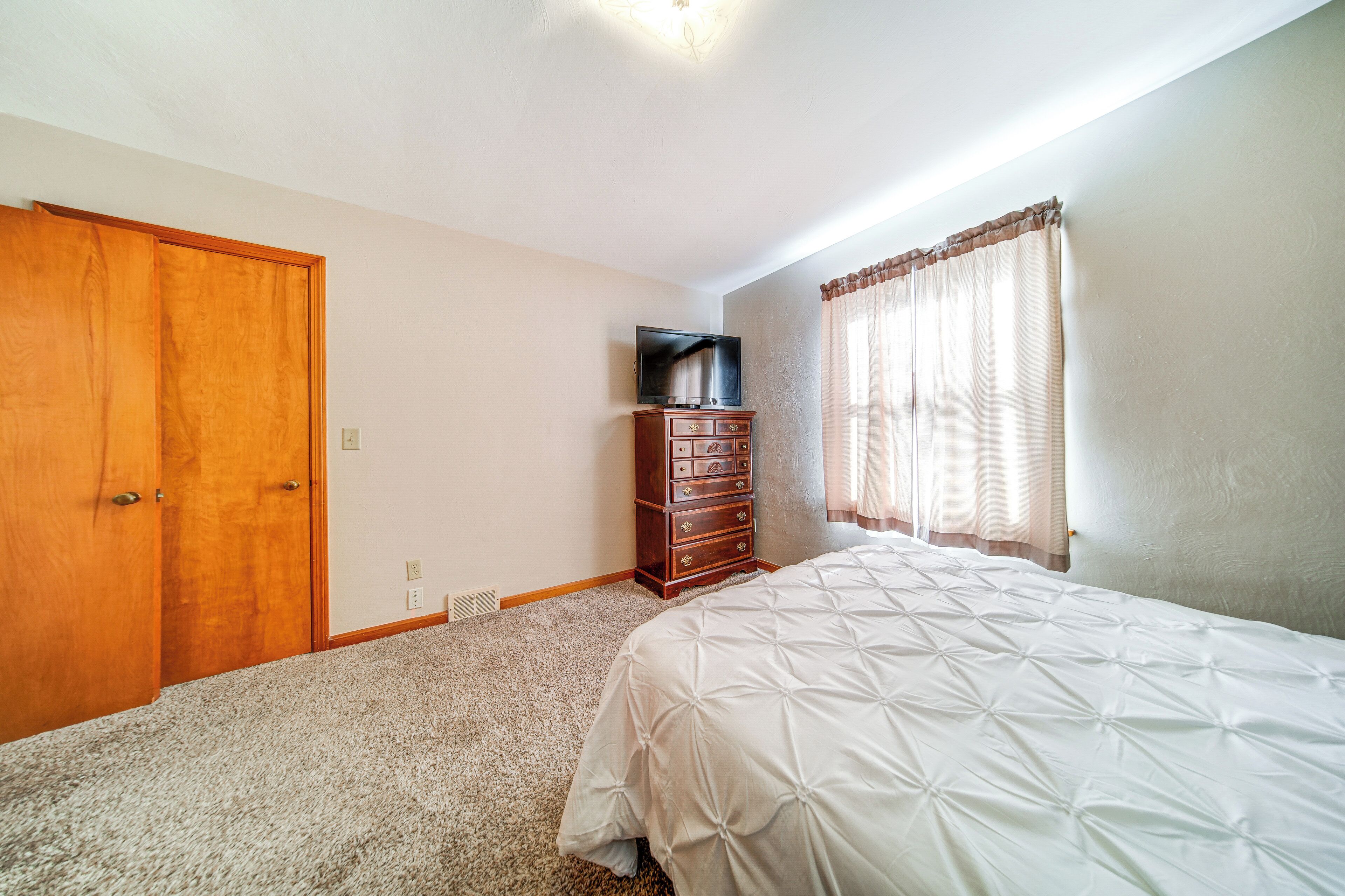 A bedroom with a bed, a dresser, a television, and a closet.