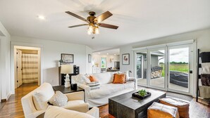 A spacious living room with a ceiling fan, a sofa set, a coffee table, and a view of the outdoors through large sliding glass doors. - Lovely Roberts Home w/ Patio & Mountain Views! (Roberts)
