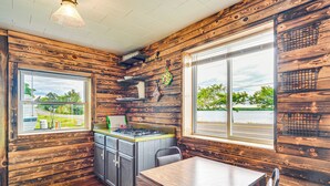 L’intérieur d’un chalet rustique, avec des murs en bois, un coin cuisine, une table à manger et de grandes fenêtres donnant sur le paysage extérieur.