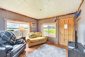 A living room with a leather sofa, a beige sofa, and a wooden floor. There is a TV on a wooden stand and a window with a view of the outside. - Wisconsin Lakeside Cottage w/ Deck, Views (Stone Lake)