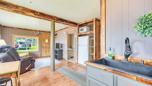 Une cuisine avec un plan de travail en bois, un évier et un four à micro-ondes. Une porte donne accès à une autre pièce.
