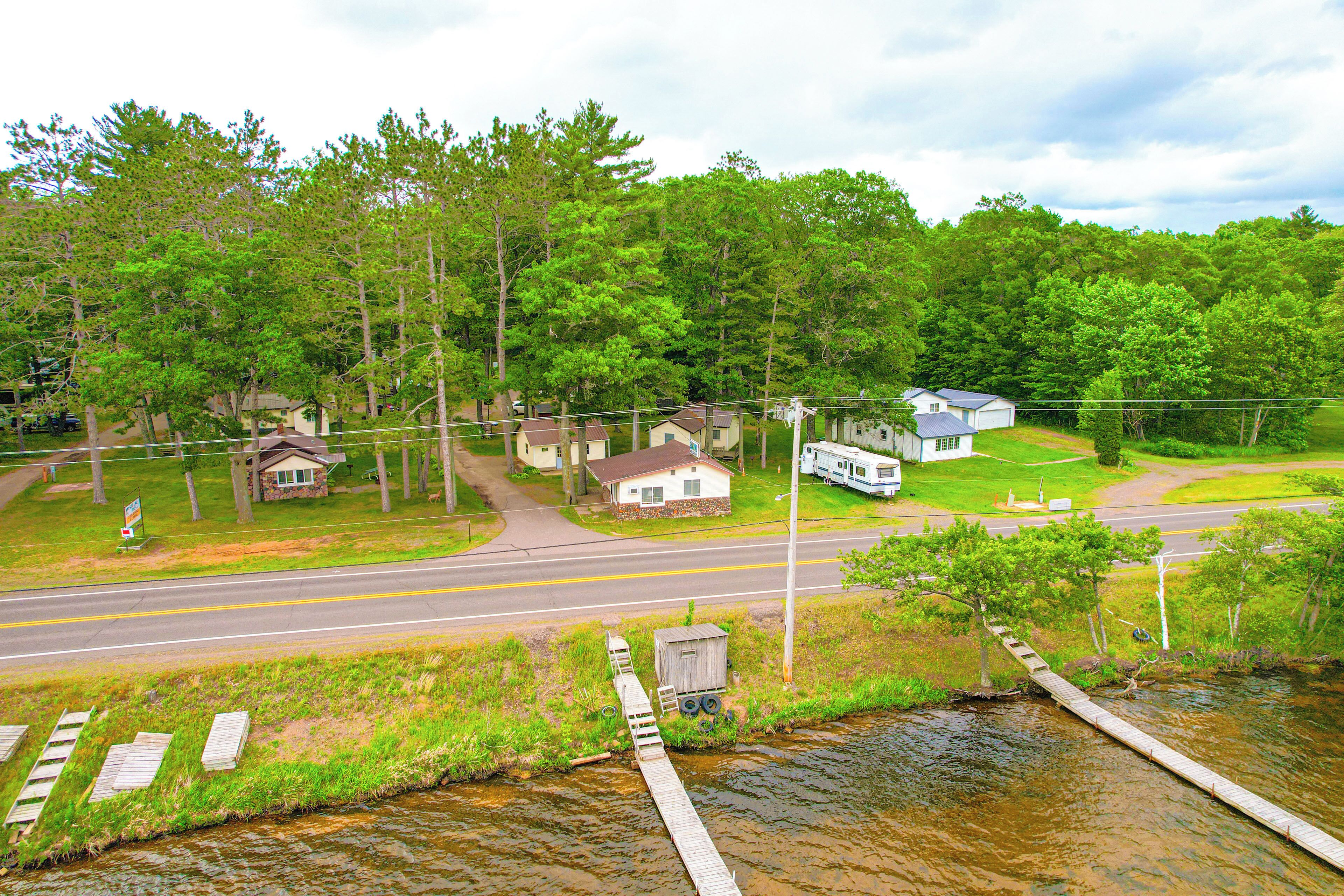 A rural landscape with a road, a wooden bridge over a stream, and houses surrounded by trees.