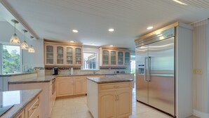 Eine moderne Küche mit hellen Holzschränken, einem Edelstahl-Kühlschrank und Pendelleuchten.