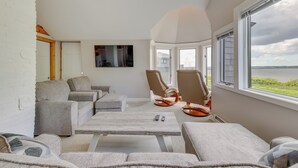 Ein modernes Wohnzimmer mit großem Fenster, grauen Sofas, einem Couchtisch und einem wandmontierten Flachbildfernseher.