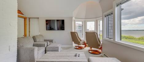 A modern living room with a large window, grey sofas, a coffee table, and a flat-screen TV mounted on the wall.